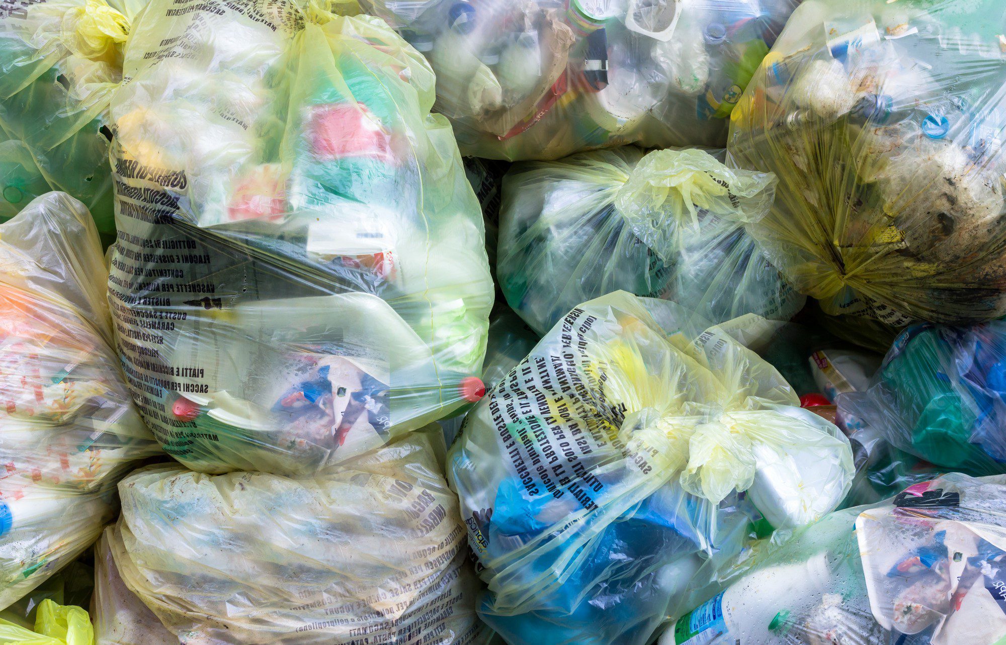 This image depicts several transparent and translucent plastic bags filled with various waste items, suggesting a collection of household trash or recycling materials. The contents appear to be mixed and include items like plastic bottles, packaging, paper, and other assorted refuse. The bags are tied shut, likely ready for disposal or processing. The image illustrates a common aspect of modern waste management practices.